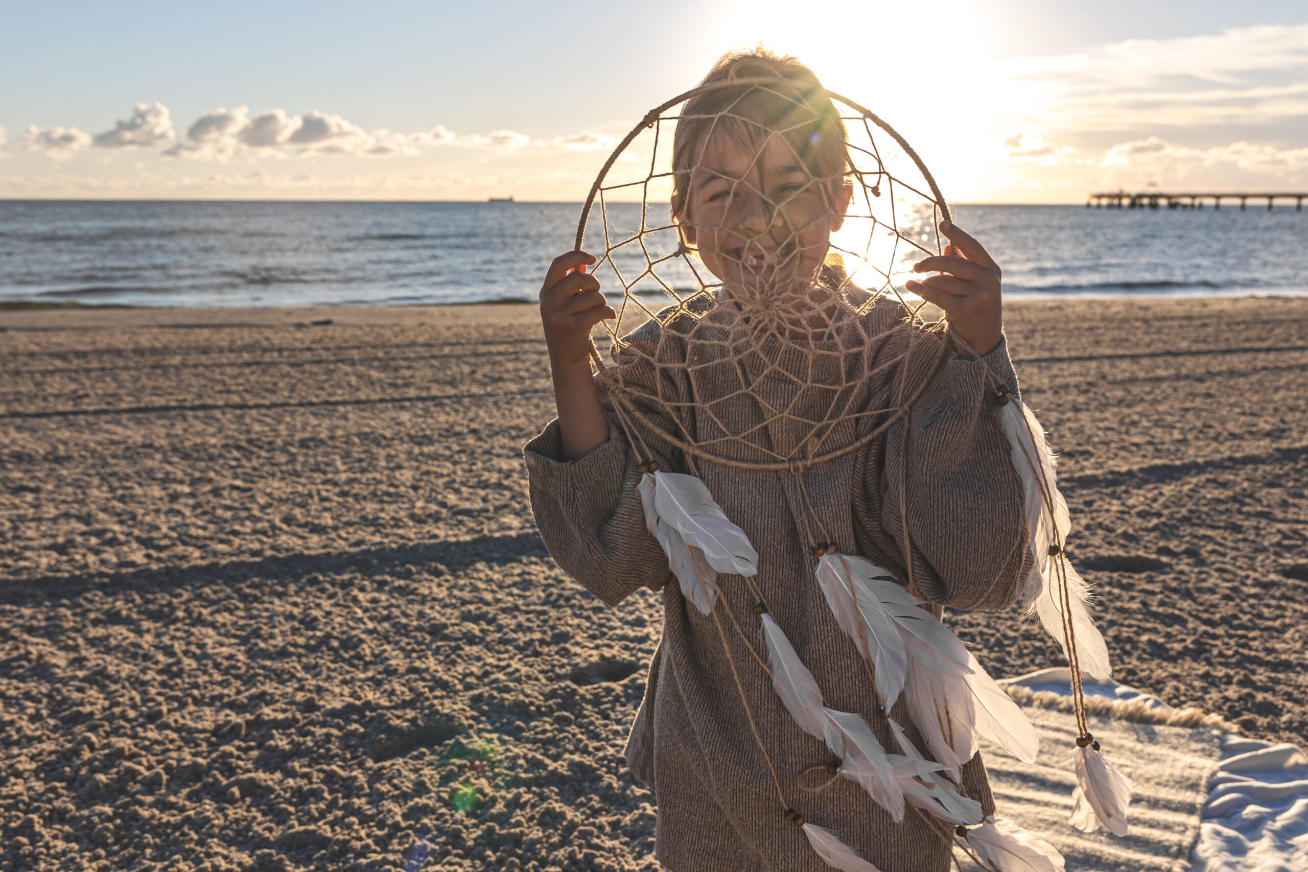 Funny little girl with a dream catcher on the seashore at sunset.